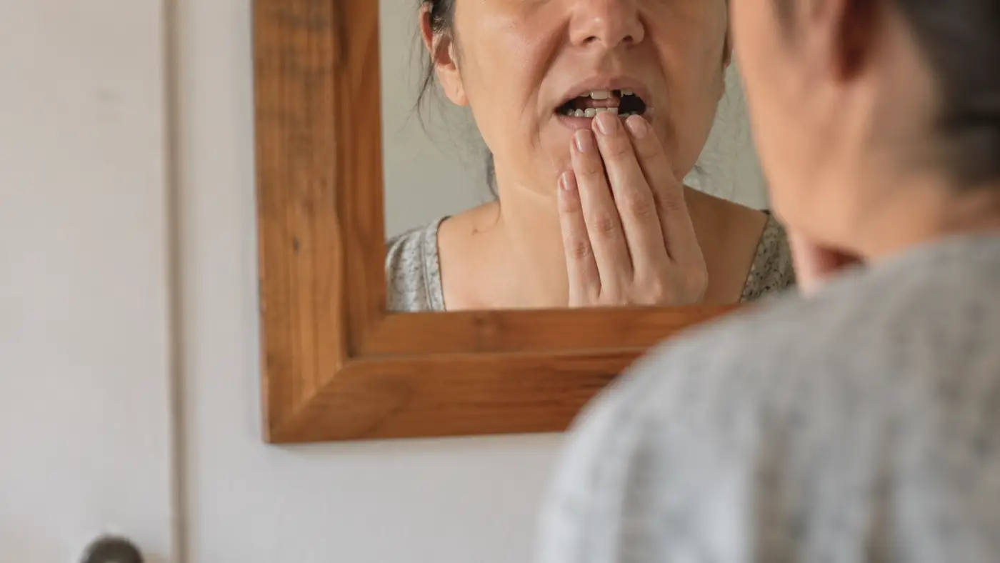 Člověk se pozerá do zrkadla a kontroluje chybějící zub, který ovlivňuje jeho istotu při úsměve a rozhovore.